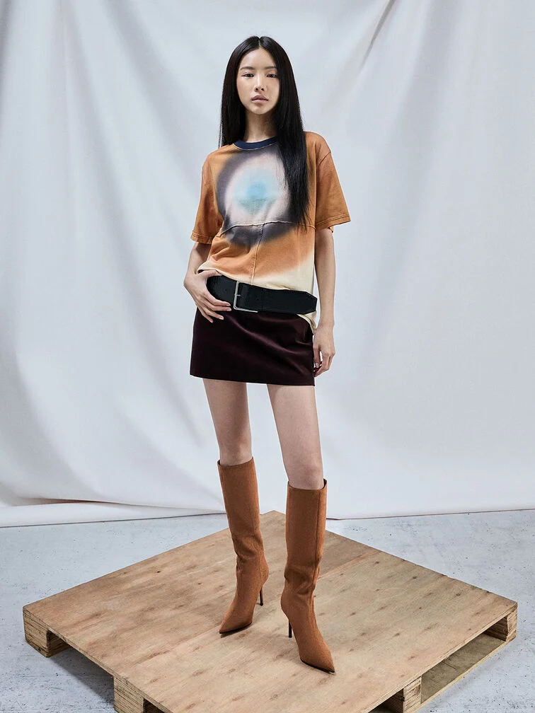 コニャックのスティレット・ニーハイブーツにミニスカートとプリントTシャツを合わせたスタイル。