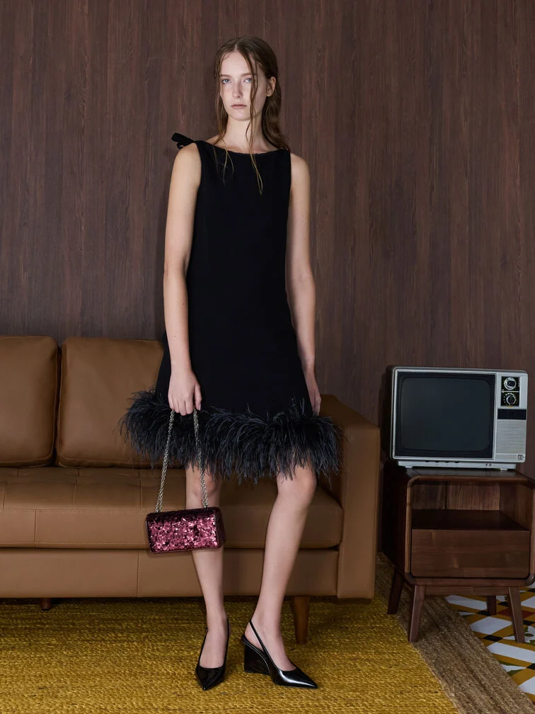 Black knee-length dress with a feather hem paired with a sequinned clutch and slingback wedges, demonstrating cocktail attire for wedding guests.  