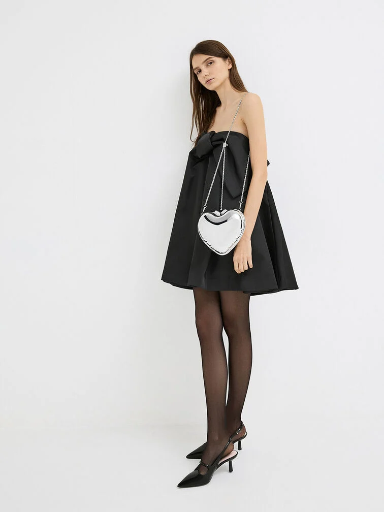 Metallic heart-shaped clutch with chain strap, styled with a black mini dress for holiday parties. 