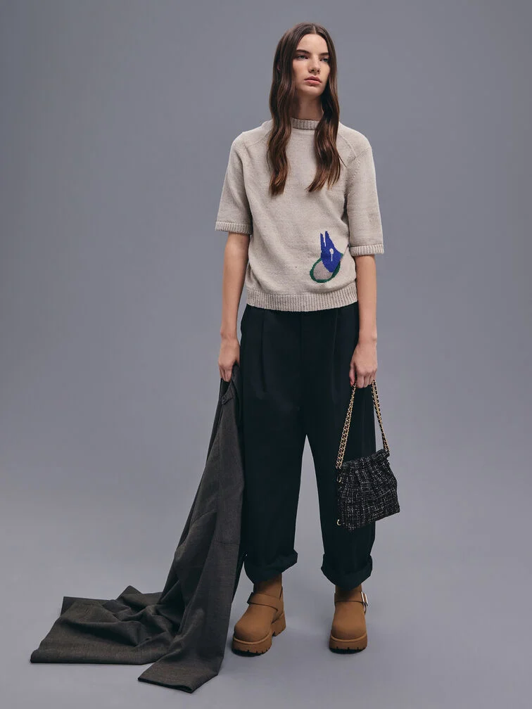 ニットTシャツと裾絞りパンツにブラウンブーツとツイードのチェーンハンドルバッグを合わせたスタイル。